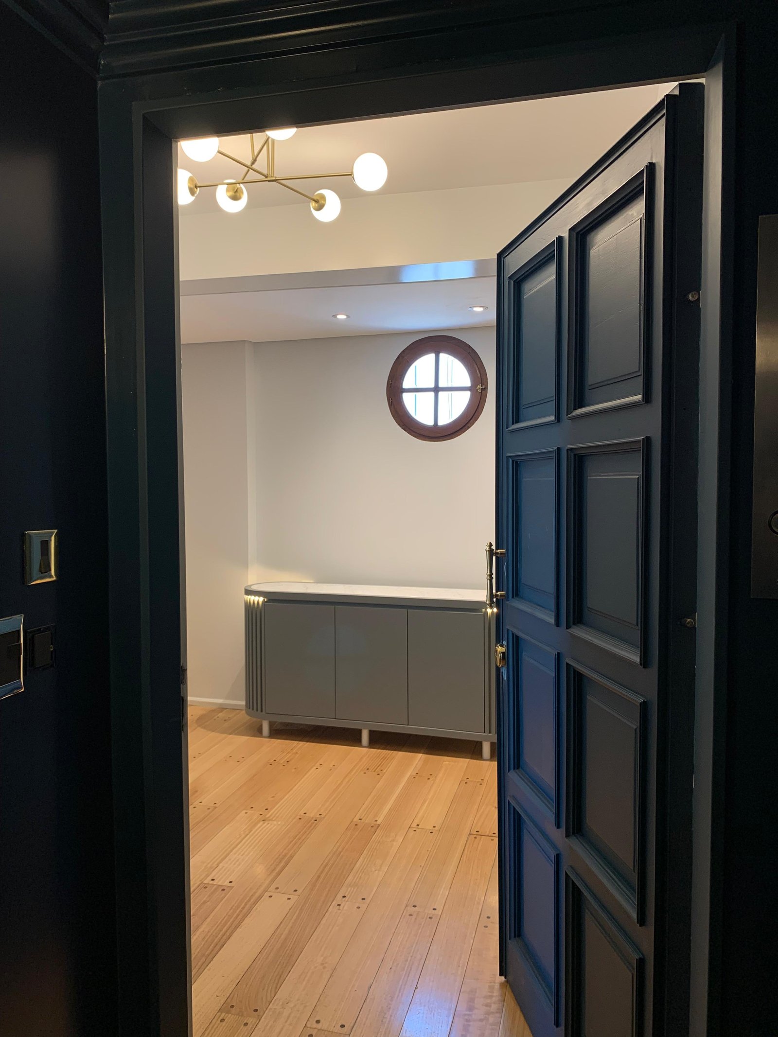 Puerta moderna negra abre a pasillo con piso de madera — proyecto 11 de Septiembre, por cromo., en Belgrano